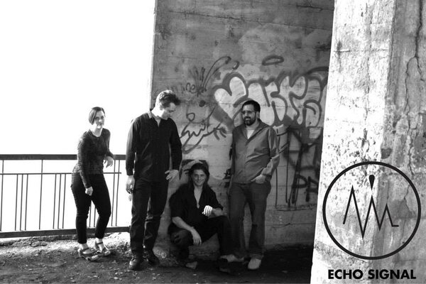 Black and white photograph of the 2014 line-up beside a graffitied bridge pillar.