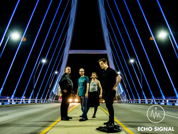 The band standing together in the middle of an empty road at night, the blue-lit cables of a bridge converging overhead.